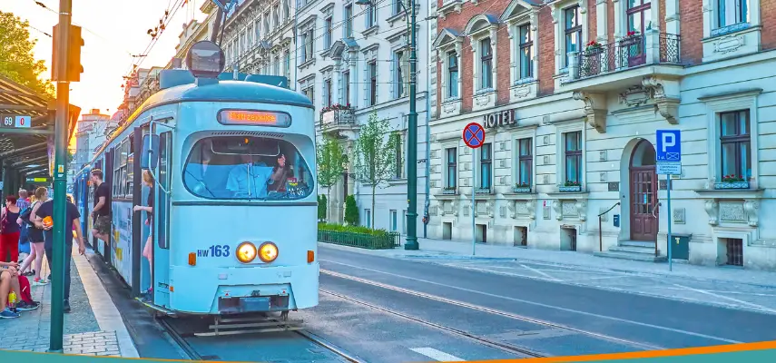 A blue tram picking up passengers on a Kraków street at sunset.