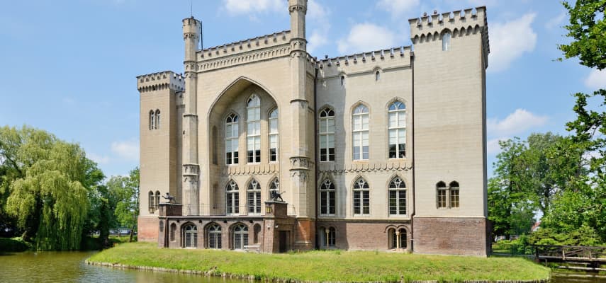 The Neo-Gothic façade of Kórnik Castle with crenellated towers and pointed arch windows, reflected in the surrounding lake.
