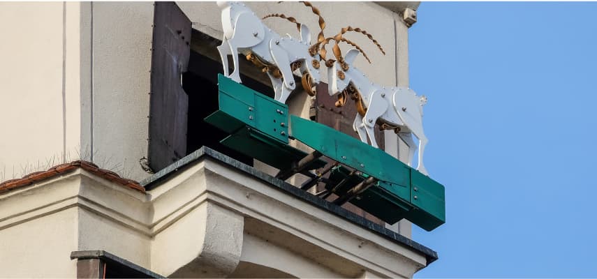 Close-up of the white mechanical goats on Poznań's Town Hall tower, mounted on their green operating platform.