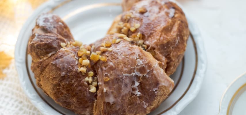 A St. Martin's croissant on a porcelain plate, glazed and topped with chopped nuts and candied fruit.